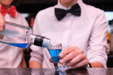 Two unrecognizable waitress serving a blue shot in a bar. They are waring bow ties.