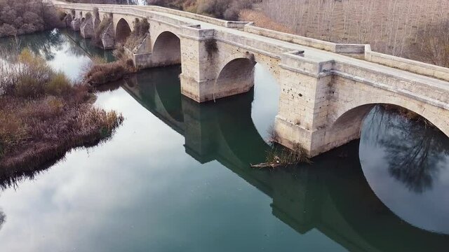 Aerial view of a medieval stone bridge over Pisuerga river in Itero del Castillo, historic village in Burgos province, Spain. High quality 4k footage