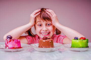Difficult choice for young beautiful girl  which cake to eat first. Funny portrait. Holiday, sweets, pleasure, food and childhood concept.  Horizontal image.