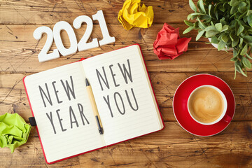 New Year 2021 goals and resolution business concept with notebook, coffee cup, crumpled paper and plant on wooden desk.