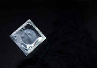 Condom and women's panties on a black background. Love and intimate relationship concept