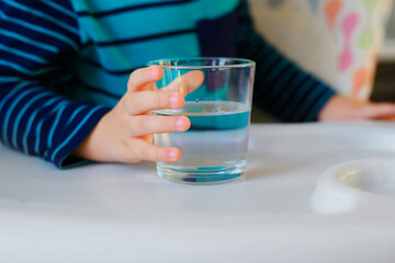 Glass of water in the hands of a child. Water balance.