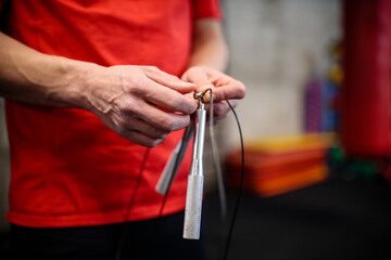Close-up of young unrecognizable Hispanic man's hands holding and adjusting jumping rope length, preparing for warm-up exercises. Healthy and active sport lifestyle