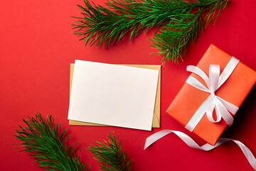 Christmas greeting card mockup with gift box and pine tree branches on red background