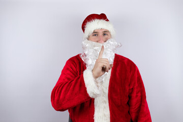 Fototapeta na wymiar Man dressed as Santa Claus standing over isolated white background asking to be quiet with finger on lips. Silence and secret concept.