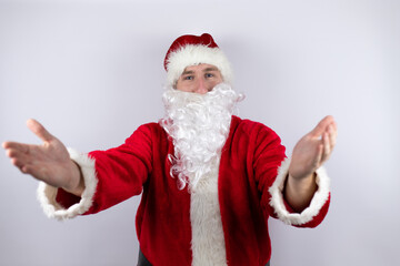 Fototapeta na wymiar Man dressed as Santa Claus standing over isolated white background looking at the camera smiling with open arms for hug