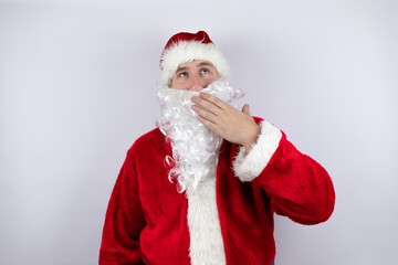 Man dressed as Santa Claus standing over isolated white background surprised covering the mouth