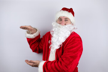 Fototapeta na wymiar Man dressed as Santa Claus standing over isolated white background gesturing with hands showing big and large size sign, measure symbol. Smiling . Measuring concept.