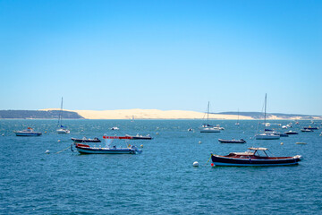 Fototapeta na wymiar Yacht boat in the blue sea in front of the sand dune in Bassin d'arcachon to visit oysters farm 