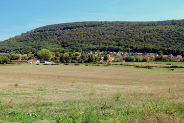 Beautiful French mountain landscape with a forest edge and a small church in the distance. Photo was taken on a summer day with blue sky.