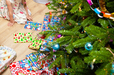 Lots of presents under a decorated christmas tree, colorful packages on the floor. Anonymous child waiting to unpack the gifts. Christmas presents heap, celebration, traditional gifting concept