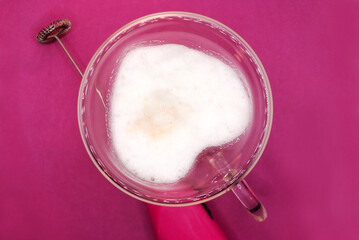 Glass cup with cappuccino on a pink background. Glass cup in the shape of a heart and double glass. Battery cappuccino machine or milk frother for making coffee at home.