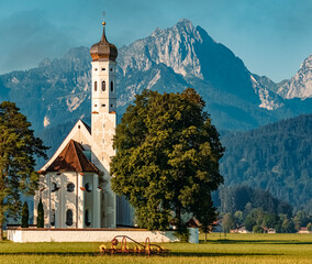 The famous church Saint Coloman with old agricultural gear and mountains in the background near...