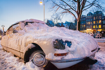 Classic car covered with snow on a winter day during sunset in Amsterdam