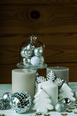 Christmas composition with candles, artificial trees, snowflakes and shiny white and gray Christmas balls on a wood background.