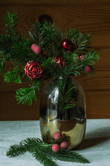 Christmas composition with fir branches, artificial flowers and berries in a vase on a wooden background.