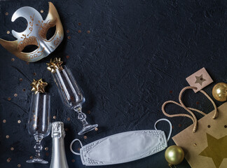 Carnival mask, wine glasses, bottle of champagne, glass Christmas balls, gift bag, protective medical mask on a black background.