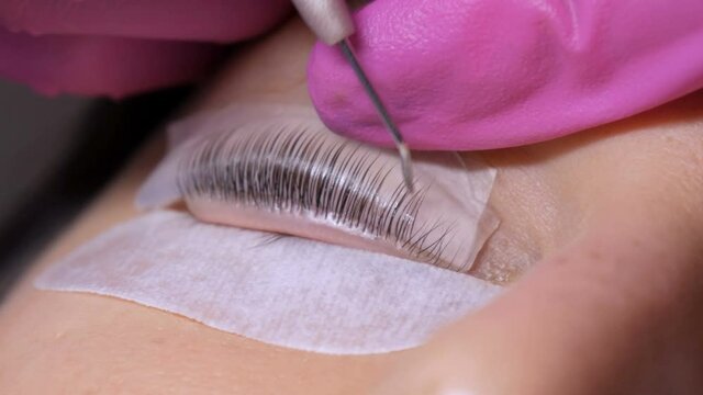 Face of a young girl before a modern eyelash lamination procedure in a professional beauty salon. The master applies special glue before the eyelash curling procedure in pink rubber gloves close up.