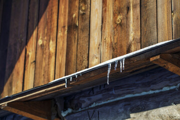 Fototapeta na wymiar Icicles on the roof of a village house on a sunny winter day.