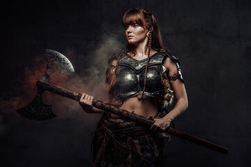 Atmospheric portrait of scandinavian amazon with brown hairs dressed in light armour holding two...