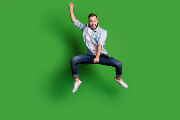 Full size photo of optimistic funky guy jump horse wear blue shirt jeans footwear isolated on green color background
