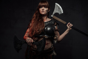 Seductive and strong scandinavian woman fighter wielding two axes and dressed in dark light armour...