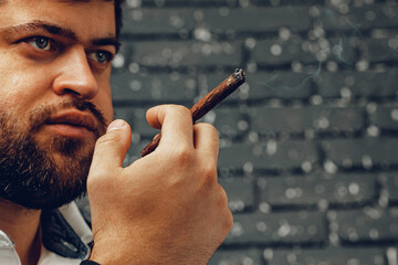 Bearded man smoking cigar against black brick wall