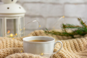 Obraz na płótnie Canvas A Cup of hot coffee with milk on a warm blanket with a garland and a sprig of spruce.Christmas concept.spruce branch on a woolen blanket.