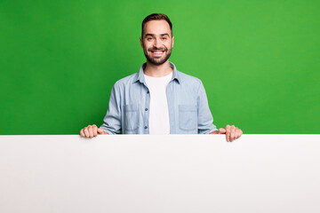 Portrait of optimistic guy show advert wear blue shirt isolated on vibrant green color background