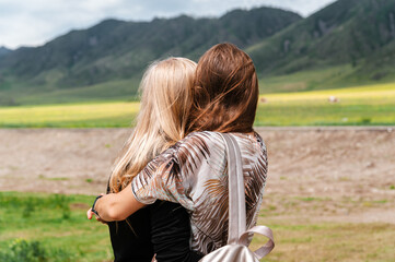 Photo of a Mountain summer Landscape. Travel location of popular tourist attraction. View of beautiful nature. Grassy field, hills and couple hugging girls on cloudy sky background.