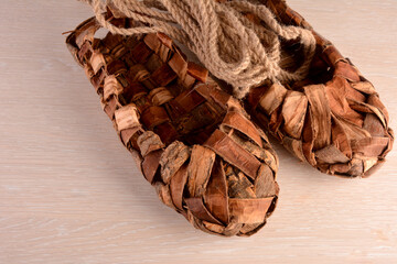 Birchen woven bast shoes hang on a log wall.