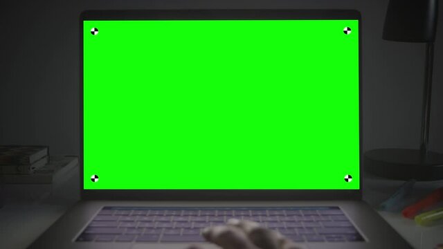 Laptop with green screen. Female hands typing and scrolling on a track pad. Dark office. Dolly in. Perfect to put your own image or video. Track with perspective corner pin.  