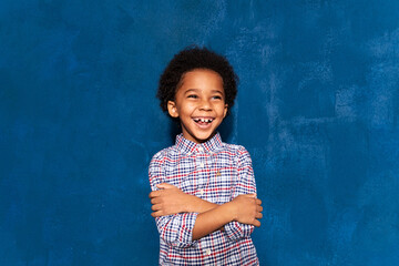 Joyful african kid boy laughing at humor joke on blue studio background, overjoyed cute black child...