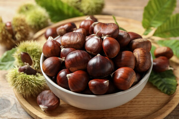 Fresh sweet edible chestnuts in bowl on wooden board