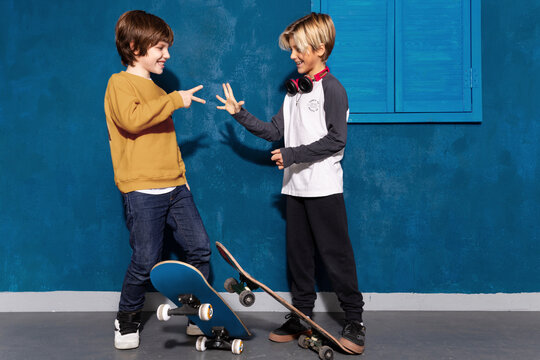 Joyful skateboarders boys playing hand game rock paper scissors together. Contemporary caucasian children, smiling schoolboys with skateboards play roshambo.