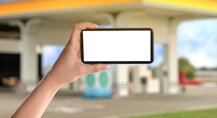 Woman paying for refueling via smartphone at gas station, closeup. Device with empty screen