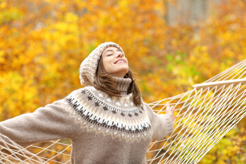 Happy woman sitting on hammock stretching arms in fall