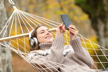 Happy woman listening to music on hammock in autumn