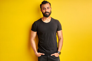 arabic man with hands in pocket looks at camera, friendly guy posing, isolated yellow background
