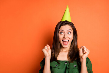 Photo of lucky lady wear green off-shoulders blouse birthday hat open mouth fists looking empty space isolated orange color background