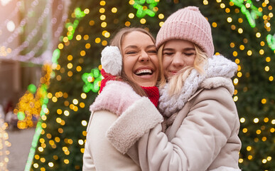 Cheerful girlfriends hugging near Christmas tree