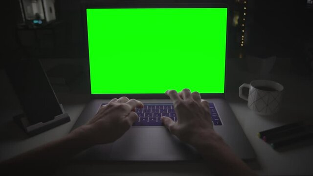Laptop with green screen. Female hands typing and scrolling on a track pad. Dark office. Locked. Perfect to put your own image or video. Track with perspective corner pin.  