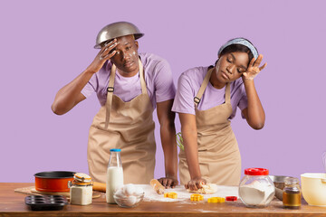 Tired black couple having trouble baking homemade cookies on violet studio background