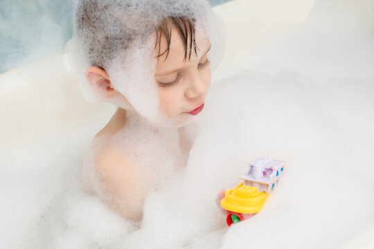 The boy plays with a boat in a bath in soapy water. Hygiene, cleanliness concept. Children's games in the bathroom.