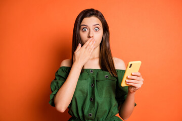 Photo of impressed girl cover mouth hold telephone wear dark shirt isolated on orange color...