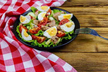 Tasty tuna salad with eggs, lettuce and fresh vegetables on wooden table