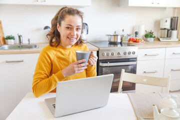 Mobile Office at home. Young woman sitting in kitchen at home working using on laptop computer. Lifestyle girl studying or working indoors. Freelance business quarantine concept.