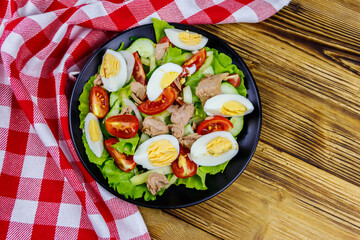 Tasty tuna salad with eggs, lettuce and fresh vegetables on wooden table. Top view