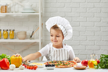 little boy in chef hat and an apron cooking pizza in the kitchen.