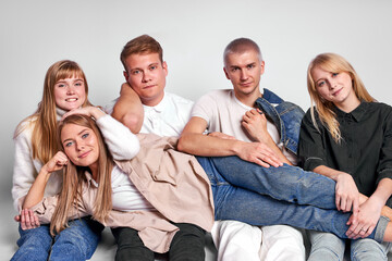 portrait of friendly caucasian guys and ladies sitting on the floor in studio, young people enjoy being together, look at camera, pleasant, wearing casual clothes